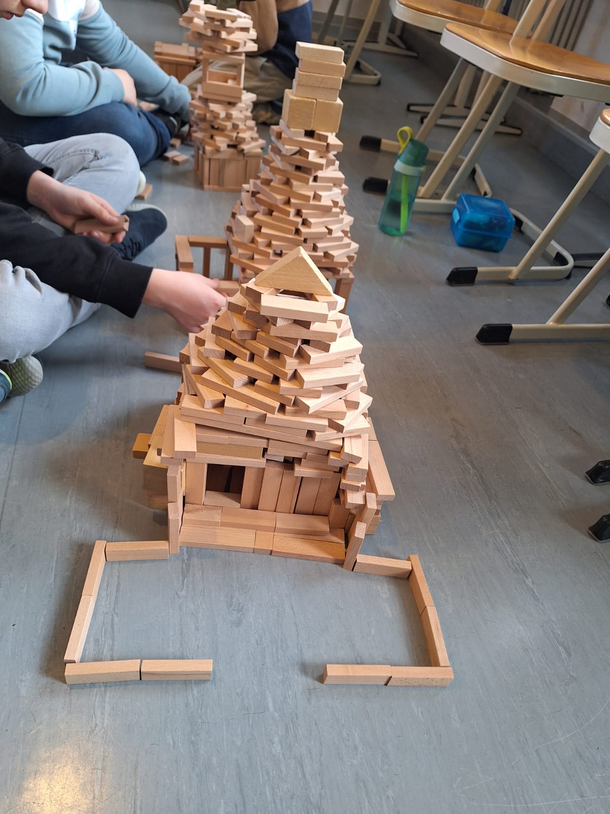 Kinder bauen eine Holzstadt aus Klötzen, mit verschiedenen Türmen und Strukturen auf dem Boden.